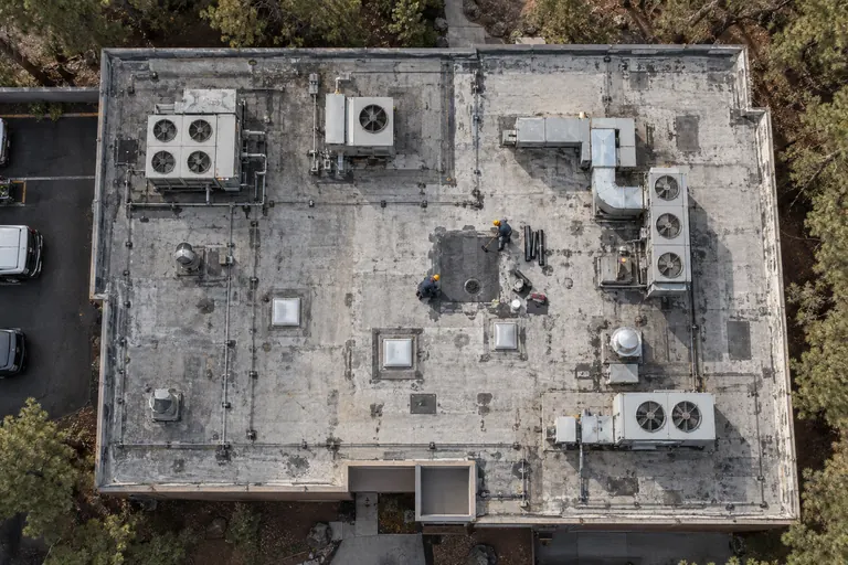 Overhead view of an aged flat commercial roof with rooftop units, skylights, and roofers at a patch area