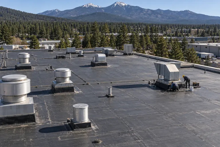 Industrial flat roof with exhaust stacks and vents and a roofer sealing a curb at a fan unit