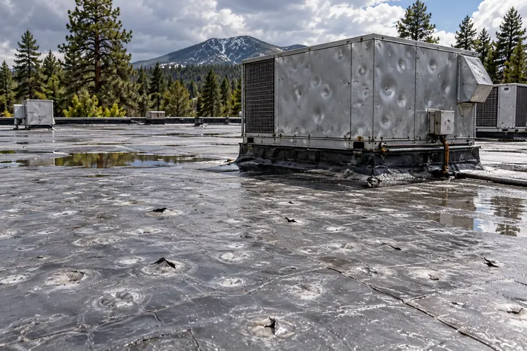 Hail-dented rooftop unit housing and a pocked, punctured flat membrane after a storm
